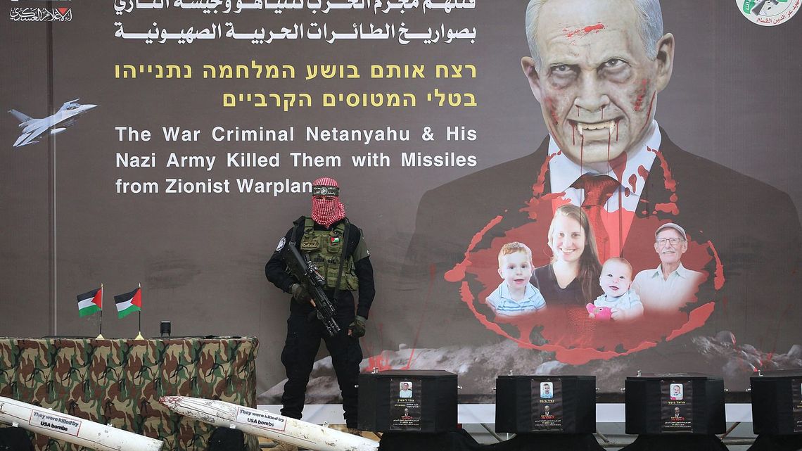 Un miliciano palestino junto a los féretros de los cuatro rehenes muertos cuyos cuerpos van a entregar a Israel. En el cartel se lee: El criminal de guerra Netanyahu y su ejército nazi los mató con misiles de aviones sionistas.