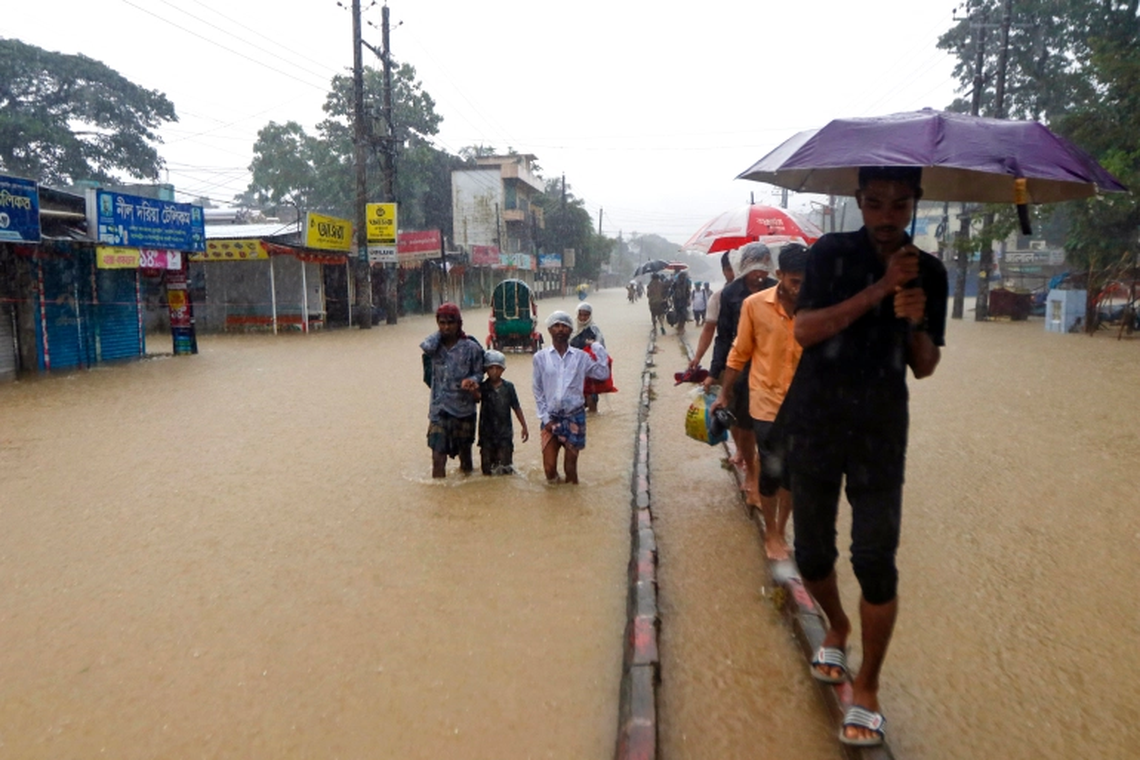 La gente vadea a lo largo de una carretera en una zona inundada tras las fuertes lluvias monzónicas.