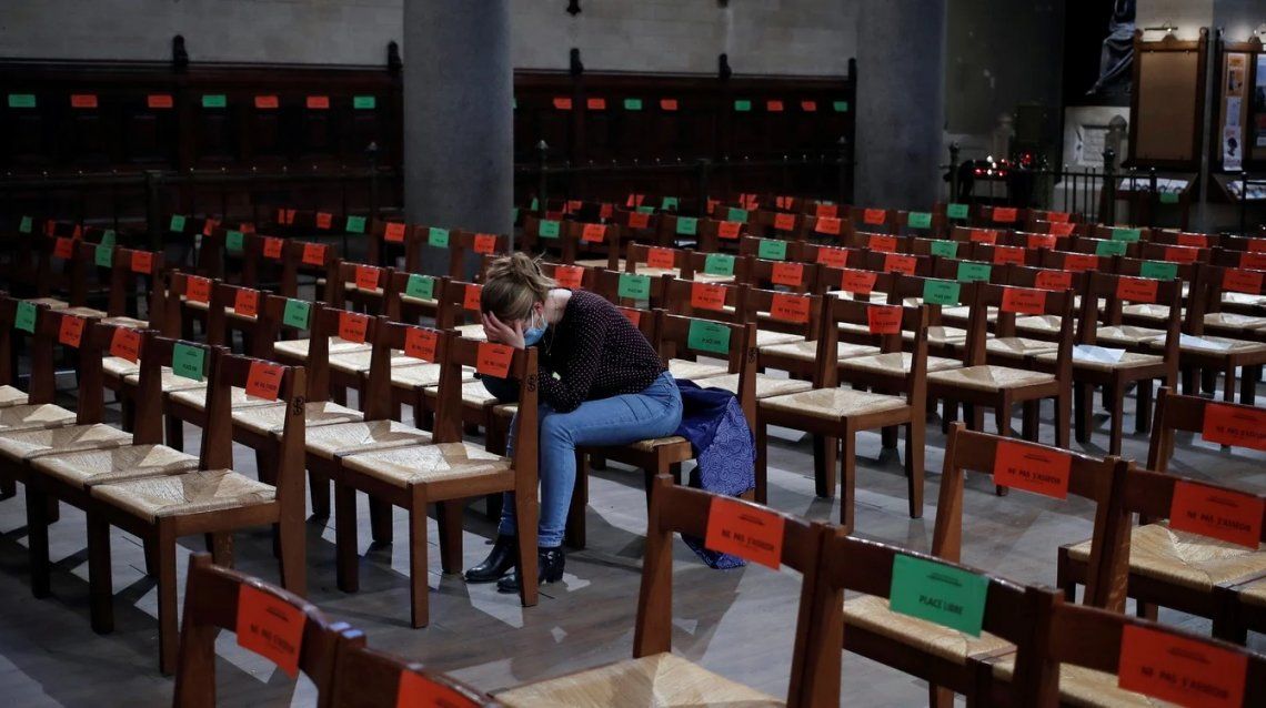 Un devoto reza mientras se colocan calcomanías para respetar el distanciamiento social en los asientos después de un servicio del Jueves Santo de Pascua en la iglesia de Saint Pierre de Montrouge